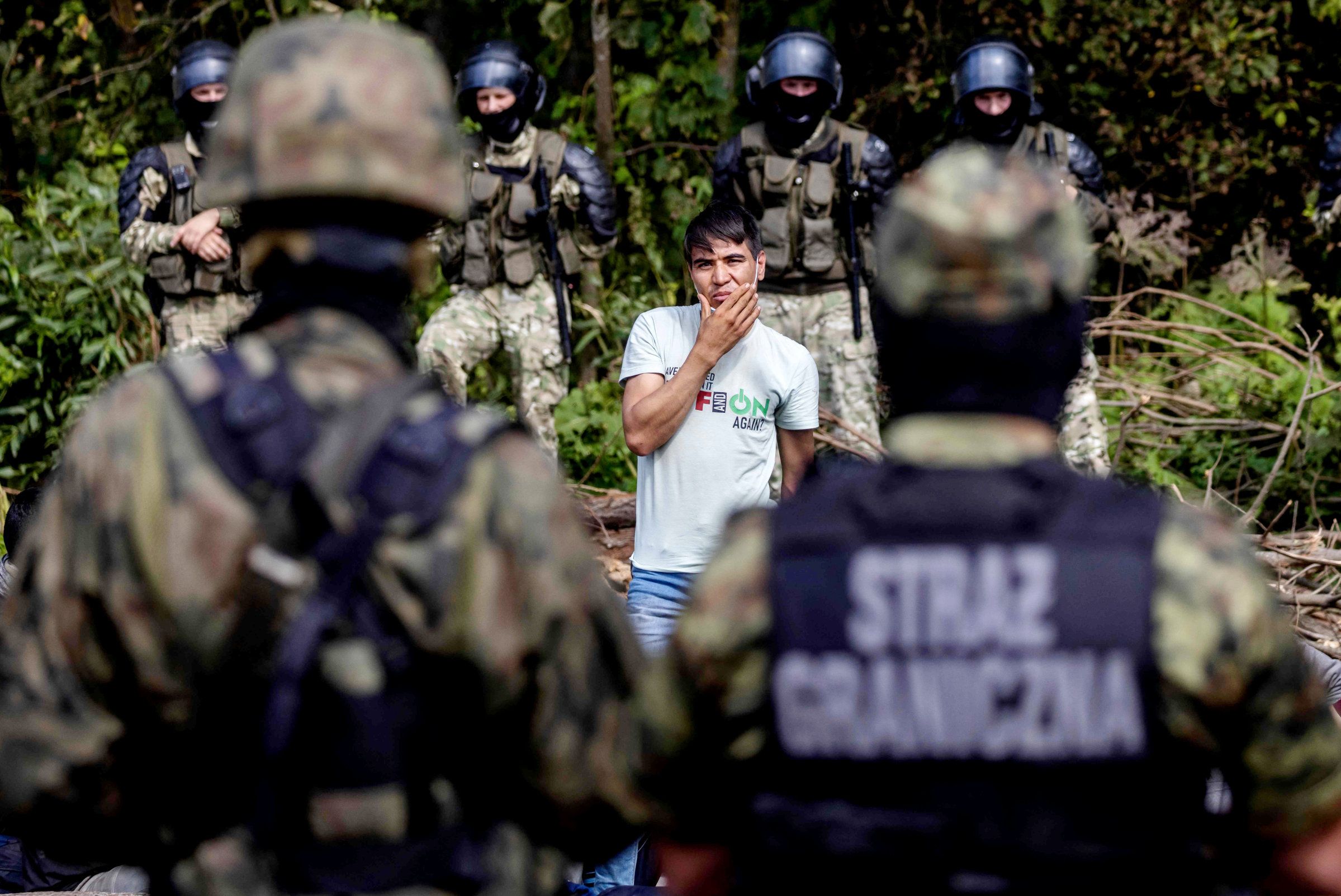 A member of a group of migrants believed to be from Afghanistan stands as he tries to confirm their will to apply for international protection in Poland in the presence of Polish volounteer lawyers, press members and Polish Parliament deputies, in the small vilage of Usnarz Gorny near Bialystok, northeastern Poland, located close to the border with Belarus, on August 20, 2021. - The fate of a group of 32 bedraggled migrants stranded at a makeshift encampment on the border between Belarus and Poland for nearly two weeks has sparked a heated debate in Poland. The sight of the migrants, who are believed to be from Afghanistan, stuck between armed Belarusian officers and Polish soldiers just a few metres away has moved many Poles. (Photo by Wojtek RADWANSKI / AFP)