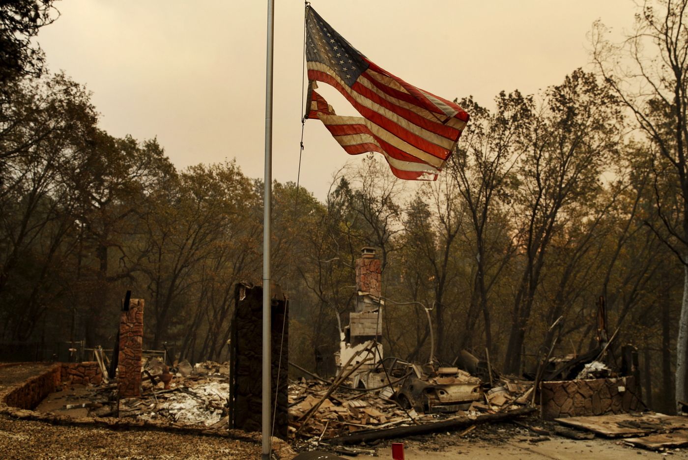 A tattered flag flies over a burned out home at the Camp Fire, Sunday, Nov. 11, 2018, in Paradise, Calif. (AP Photo/John Locher)
