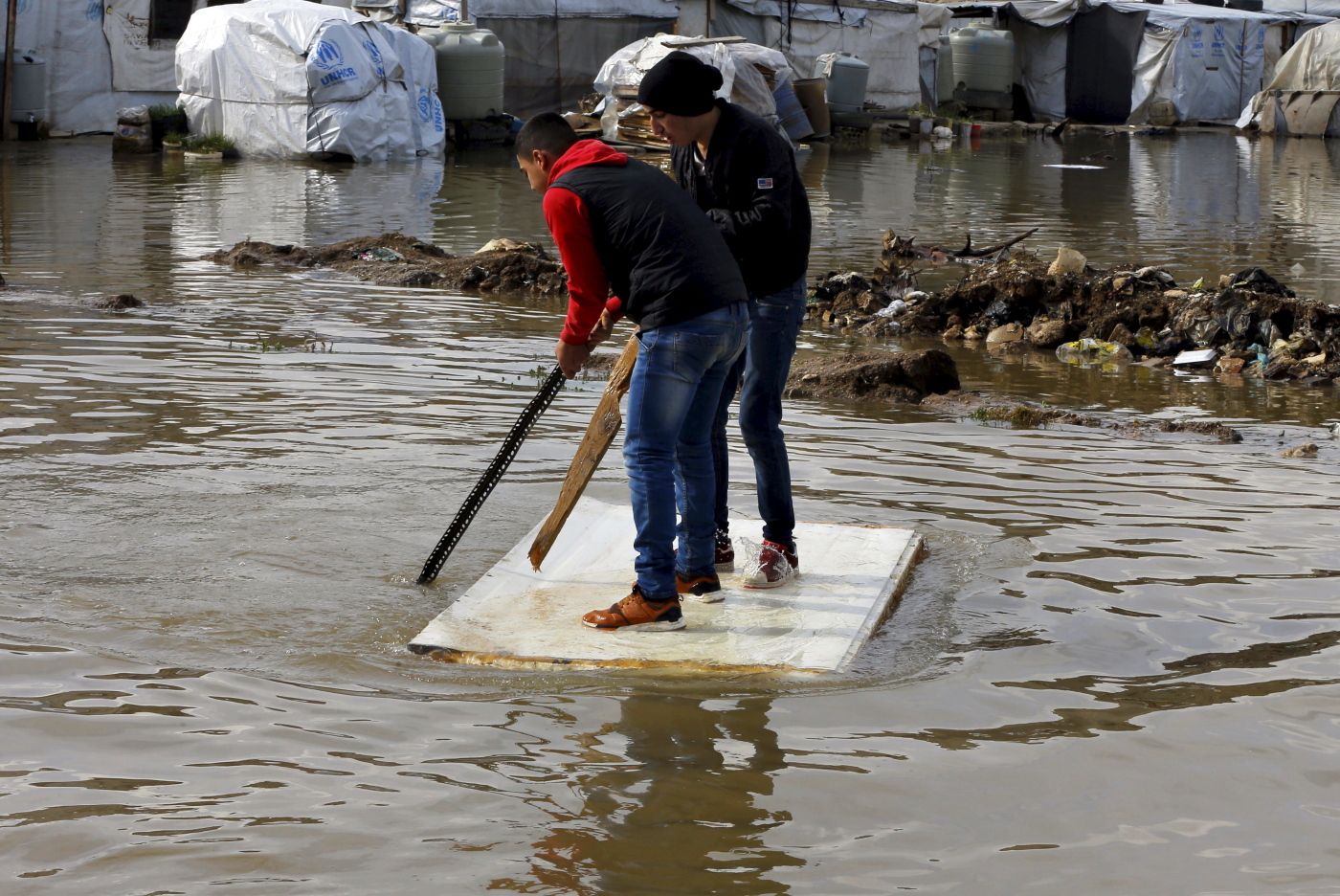 Syrian refugees use a floating piece of wood to move around after heavy rain caused flooding at a refugee camp in the town of Bar Elias, in the Bekaa Valley, Lebanon, Thursday, Jan. 10, 2019. A storm that battered Lebanon for five days has displaced many Syrian refugees after their tents got flooded with water or destroyed by snow. (AP Photo/Bilal Hussein)