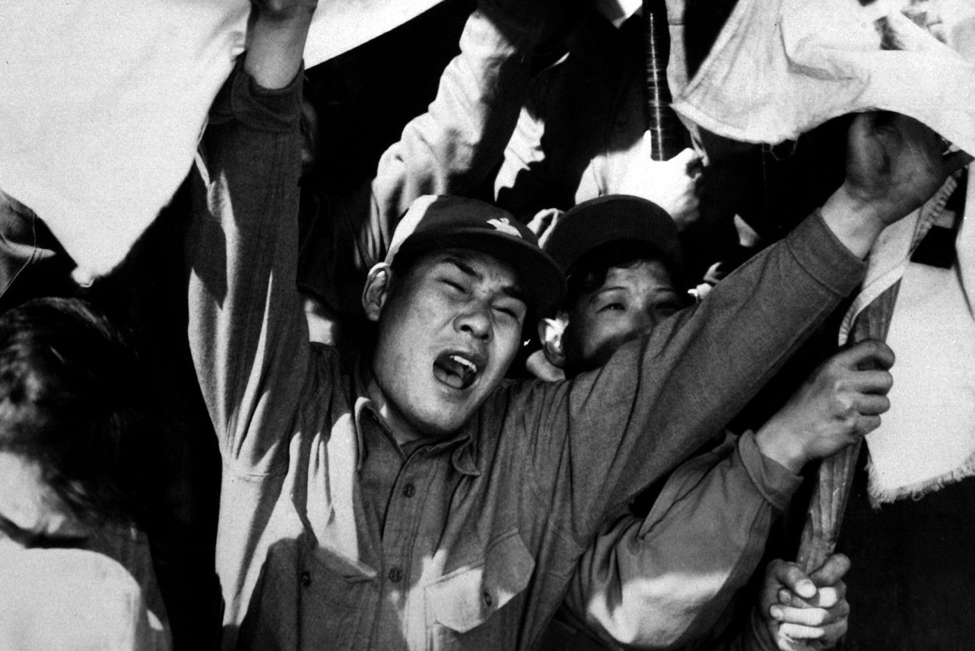 This anti-Communist North Korean just released from a prisoner of war camp is serving as a kind of cheerleader for fellow ex-POW's as they shout their joy of reaching Seoul.  The flags are of the Republic of South Korea.  Ca. 1953-54.  Gravy. (USIA) 
 Exact Date Shot Unknown 
 NARA FILE #:  306-PS-54-1497 
 WAR & CONFLICT BOOK #:  1497