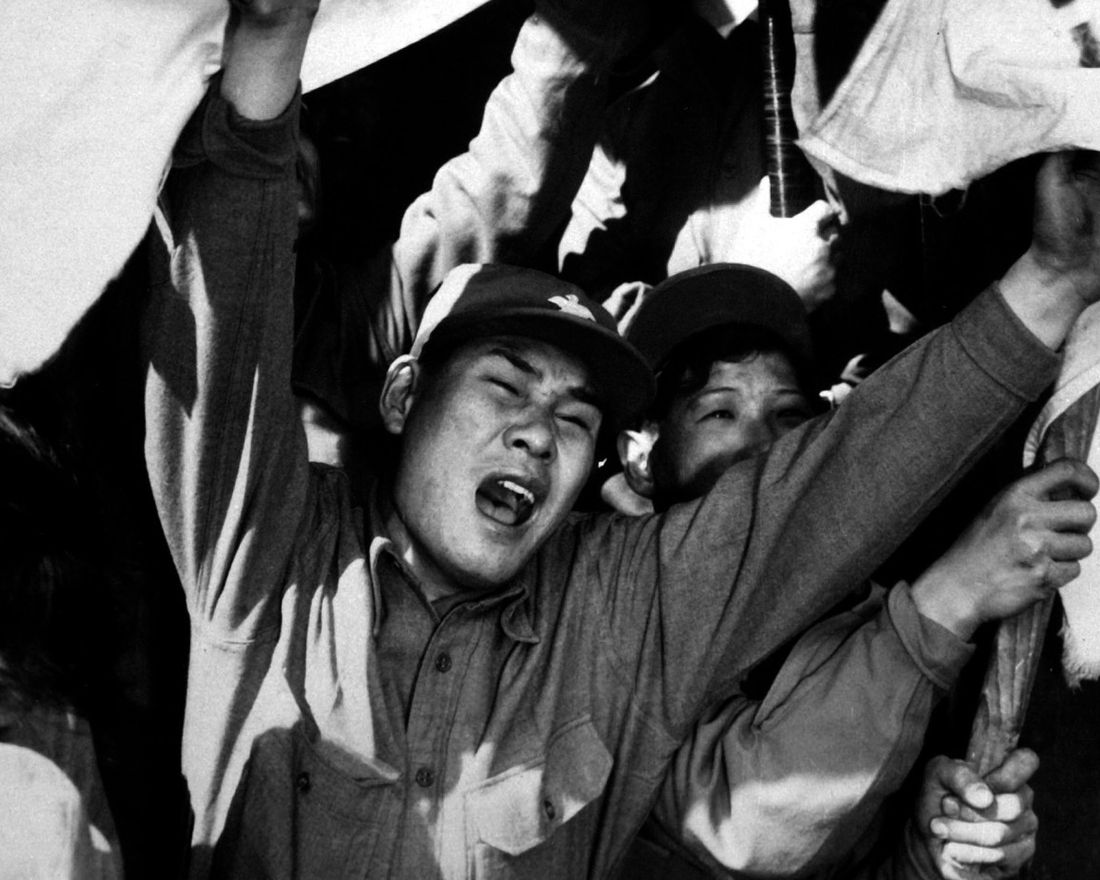 This anti-Communist North Korean just released from a prisoner of war camp is serving as a kind of cheerleader for fellow ex-POW's as they shout their joy of reaching Seoul.  The flags are of the Republic of South Korea.  Ca. 1953-54.  Gravy. (USIA) 
 Exact Date Shot Unknown 
 NARA FILE #:  306-PS-54-1497 
 WAR & CONFLICT BOOK #:  1497