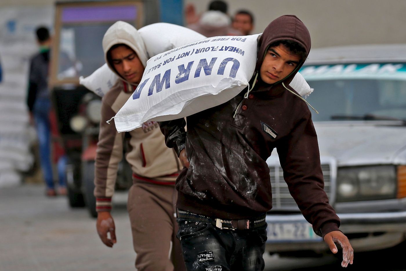 Palestinian men transport bags of flour outside an aid distribution centre run by the United Nations Relief and Works Agency (UNRWA), in Rafah in the southern Gaza Strip, on December 20, 2018. - The United Nations urged donor states to give $350 million in aid for Palestinians in 2019, saying it needed more but had to be "realistic" following swathing US cuts. The UN said the appeal, down from $539 million in 2018, was due to a lack of available donor funds across the globe. (Photo by SAID KHATIB / AFP)