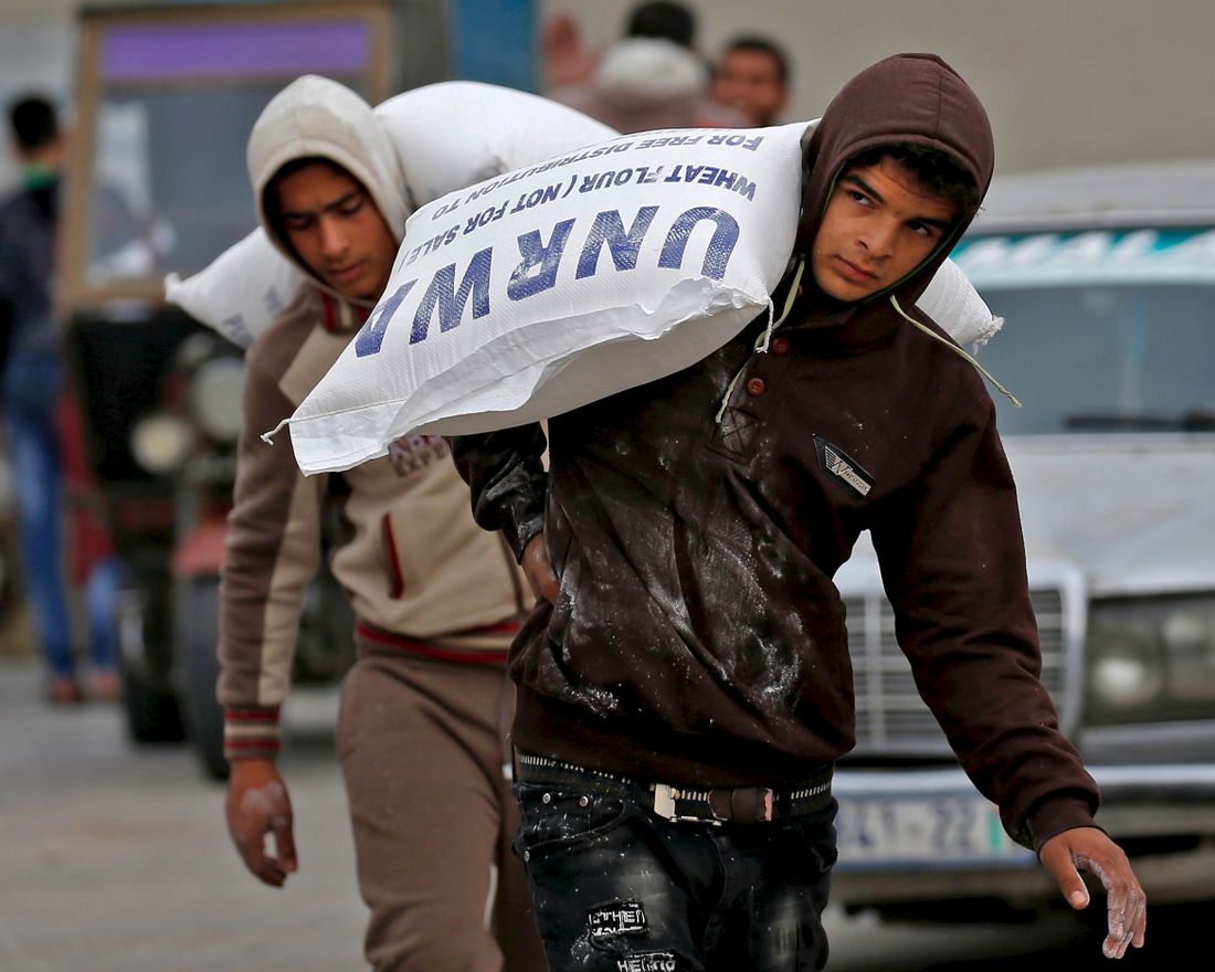 Palestinian men transport bags of flour outside an aid distribution centre run by the United Nations Relief and Works Agency (UNRWA), in Rafah in the southern Gaza Strip, on December 20, 2018. - The United Nations urged donor states to give $350 million in aid for Palestinians in 2019, saying it needed more but had to be "realistic" following swathing US cuts. The UN said the appeal, down from $539 million in 2018, was due to a lack of available donor funds across the globe. (Photo by SAID KHATIB / AFP)
