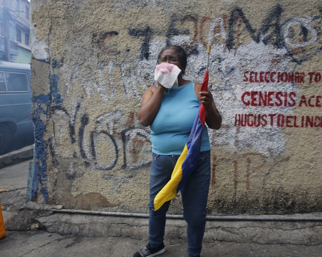 An anti-government protester affected by tear gas, fired by security forces, holds a Venezuelan flag during a show of support for an apparent mutiny by a national guard unit in the Cotiza neighborhood of Caracas, Venezuela, Monday, Jan. 21, 2019. (AP Photo/Ariana Cubillos)