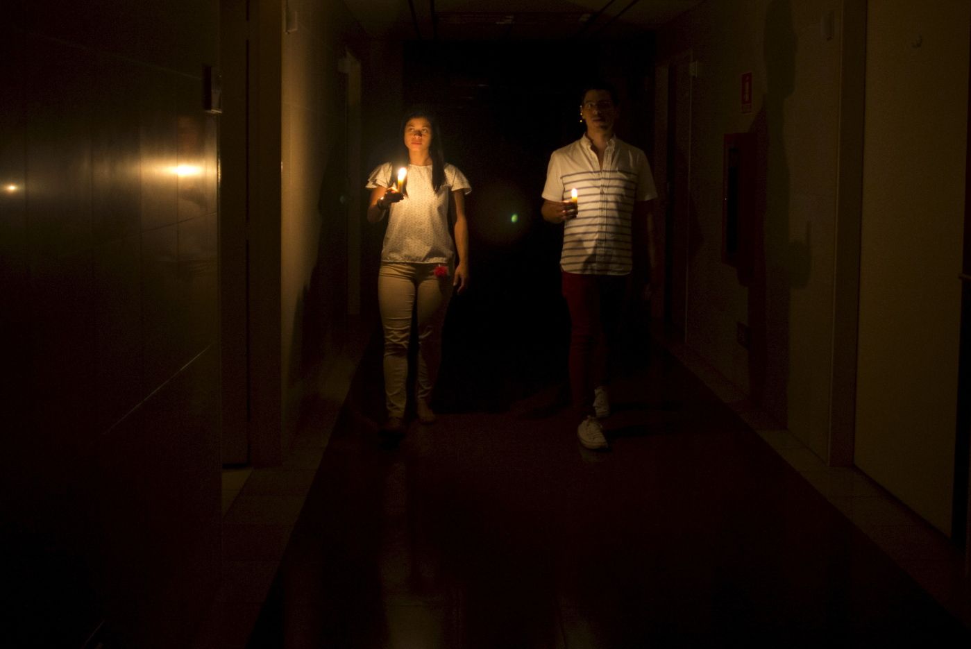 Relatives of a patient walk in the darkened hall of a clinic with a candle lighting the way, during a power outage in Caracas, Venezuela, Thursday, March 7, 2019. A power outage left much of Venezuela in the dark early Thursday evening in what appeared to be one of the largest blackouts yet in a country where power failures have become increasingly common. (AP Photo/Ariana Cubillos)