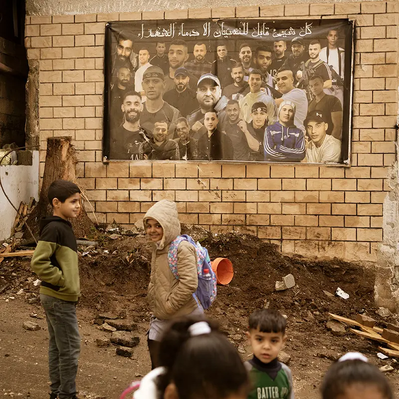 Tulkarem, Vestbredden, 11. januar Skolebarn er på vei hjem, i en by der det ikke er mange alternativer å velge mellom hva gjelder veivalg i livet. Her preges barndommen av israelske droner som hamrer byen fra luftet og bakkestyrker fra IDF er stadig inne i byen. I bakgrunnen henger en plakat med bilder av dem som har mistet livet i motstandskampen. «Alt kan bli glemt, bortsett fra martyrenes blod», lyder teksten. Foto: Christopher Olssøn