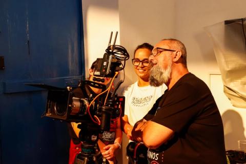 Diretor ao lado de câmera profissional com produtoras ao fundo.