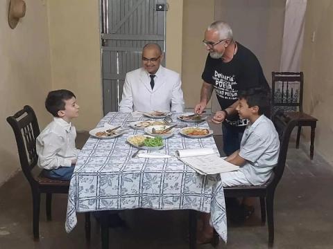 Família sentada à mesa para refeição em ambiente simples.