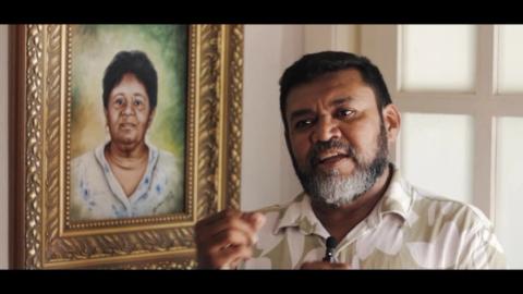 Homem falando em frente a quadro retratando uma mulher.