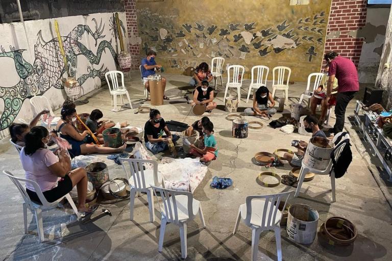 Grupo de pessoas sentadas, pintando e criando tambores.