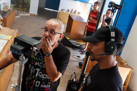 Diretor ao lado de monitor de câmera com técnico de fones e headset.