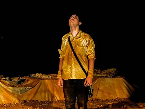 Ator de camisa amarela olha para cima, expressão pensativa.