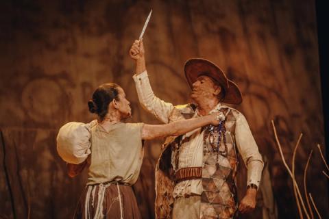 Dois atores em cena dramática, um com faca outro com colar na mão.