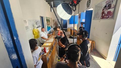 Equipe filma cena em corredor de museu entre vitrines e portas azuis.