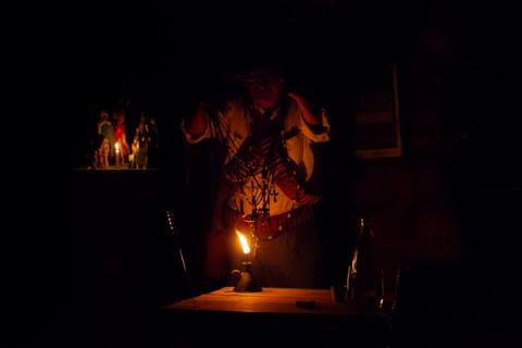 Pessoa iluminada por vela em ambiente escuro, vestindo trajes tradicionais.