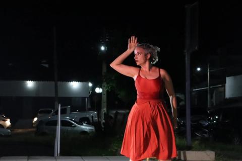 Bailarina em vestido vermelho dançando sob luz de rua, com gestos expressivos.