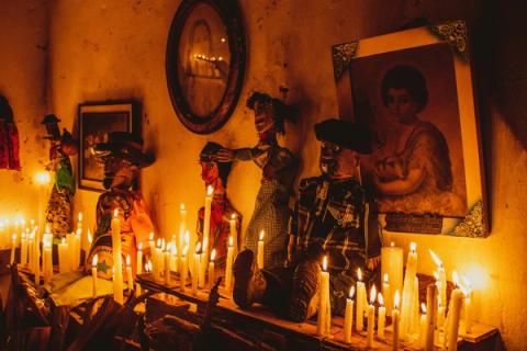 Altar decorado com bonecos tradicionais e velas acesas, sob luz amarelada.