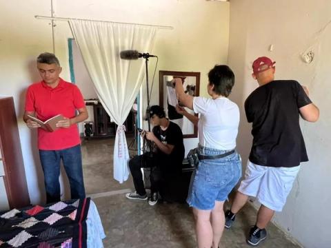 Grupo filmando dentro de casa, com um homem lendo enquanto outros gravam.