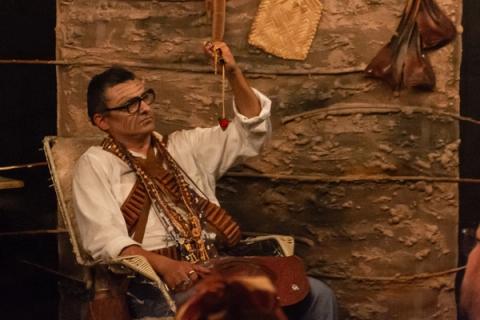 Ator sentado, segurando um objeto com uma corrente e olhando para cima.