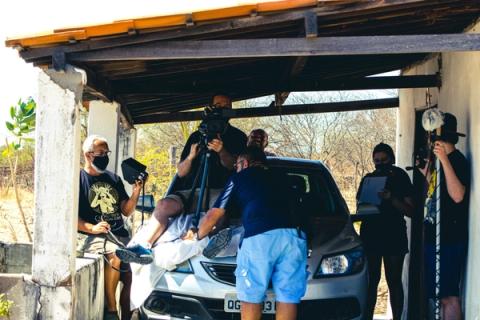 Equipe filmando cena com operador de câmera sobre carro.