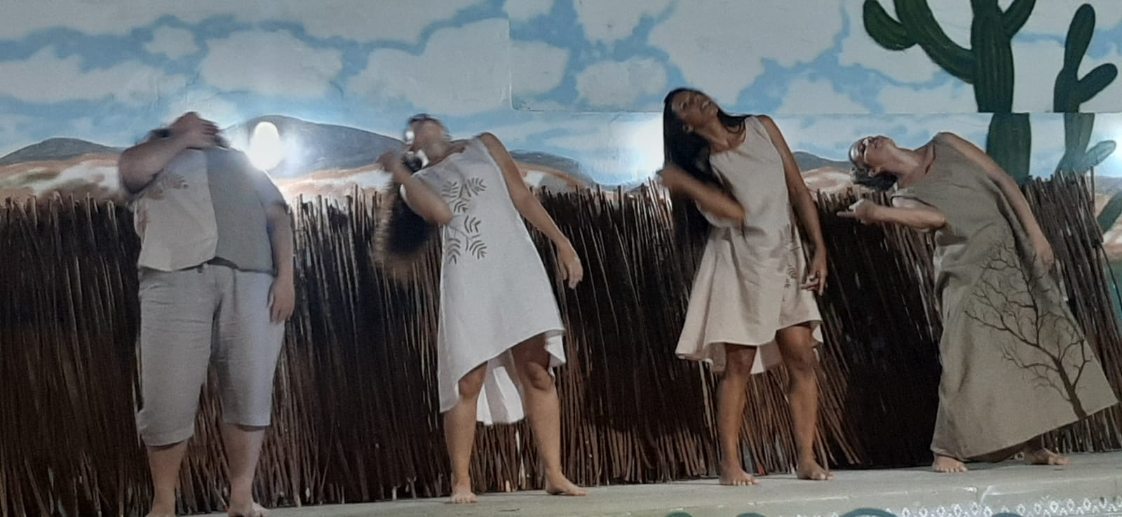 Grupo com quatro bailarinas dançando com cenário sertanejo ao fundo.