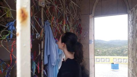 Mulher observando fitas coloridas penduradas, paisagem montanhosa ao fundo.