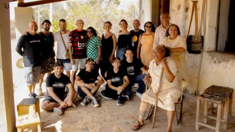 Grupo posando ao ar livre, mulher sentada e outros ao redor.