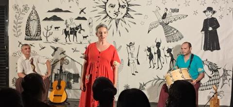 Três artistas com instrumentos em um palco decorado com motivos culturais diante do público.