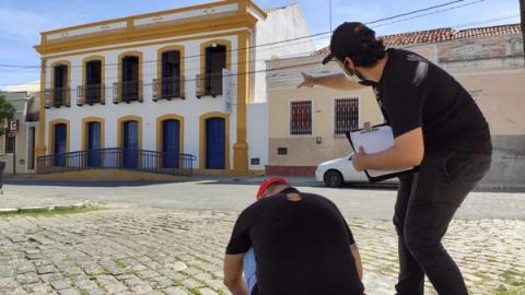 Homem apontando para um prédio amarelo enquanto outro observa.