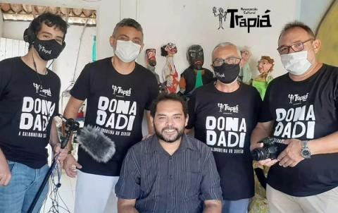 Grupo de filmagem posa para foto com bonecos ao fundo.