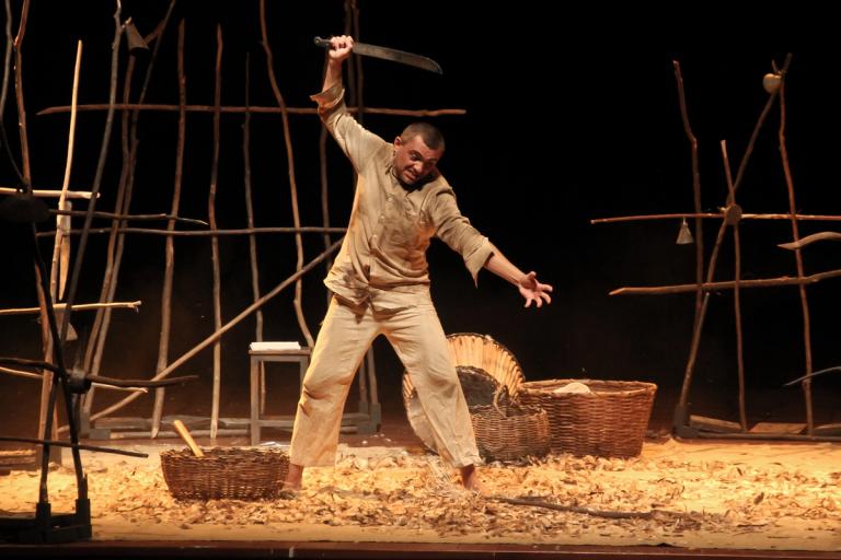 Ator erguendo faca acima da cabeça, postura dinâmica e tensa.