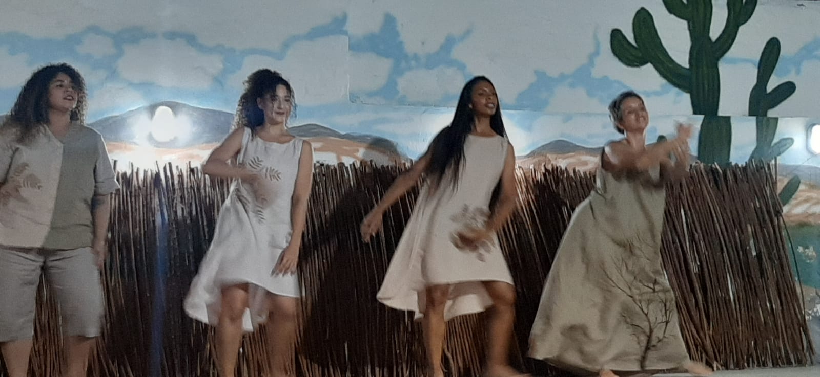 Grupo com quatro bailarinas dançando com cenário sertanejo ao fundo.