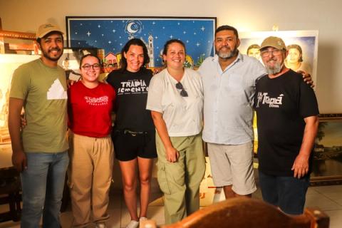 Foto de grupo com seis membros da equipe e colaboradores do filme, sorrindo e posando juntos em um ambiente interno com quadros ao fundo.