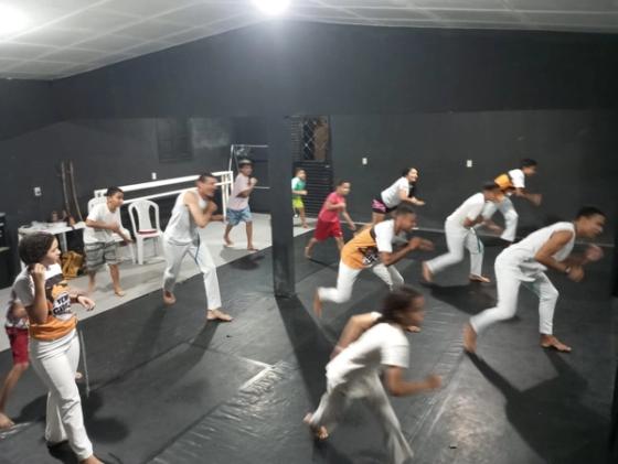 Grupo de pessoas praticando capoeira em uma sala.
