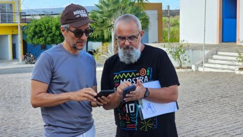 Dois membros da equipe consultam celulares em calçada de pedra.