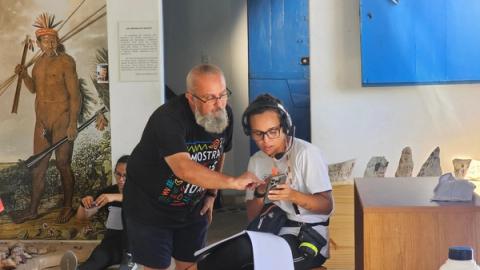 Diretor aponta para tela de celular de profissional técnico sentado.