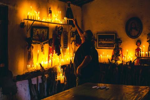 Pessoa acendendo velas em um altar com bonecos e imagens religiosas.