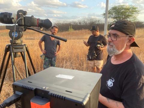 Grupo observando gravação em campo aberto.
