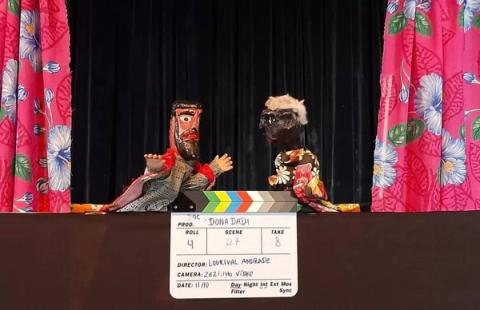 Bonecos de marionetes em palco com cortinas floridas e clapperboard.