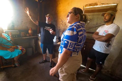 O diretor gesticula enquanto dá instruções à equipe e ao elenco em um set de filmagem com aparência rústica, durante a produção de uma cena.