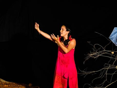 Atriz em vestido vermelho gesticula intensamente na cena.