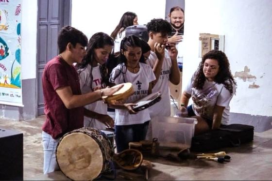 Grupo de jovens tocando instrumentos musicais em sala.