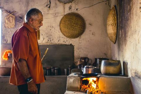 Homem cozinhando em fogão a lenha em cozinha rústica.