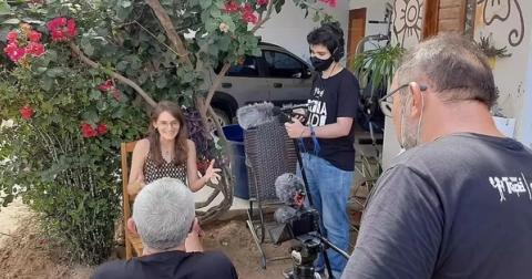 Grupo filmando entrevista em ambiente externo, com flores ao fundo.