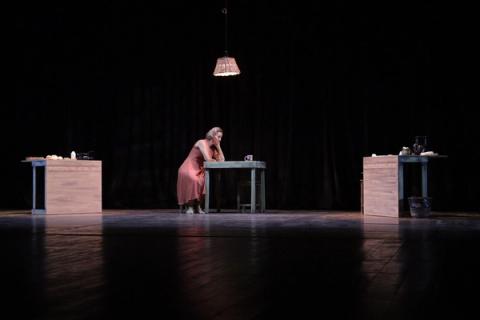 Bailarina em vestido vermelho, em cena com lâmpada pendente e fundo escuro.