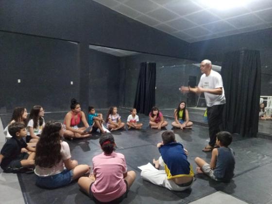 Professor conversando com grupo de crianças sentadas no chão.