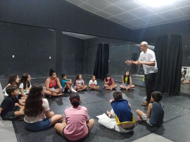 Professor conversando com grupo de crianças sentadas no chão.