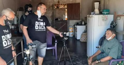 Equipe gravando homem sentado em cozinha simples.