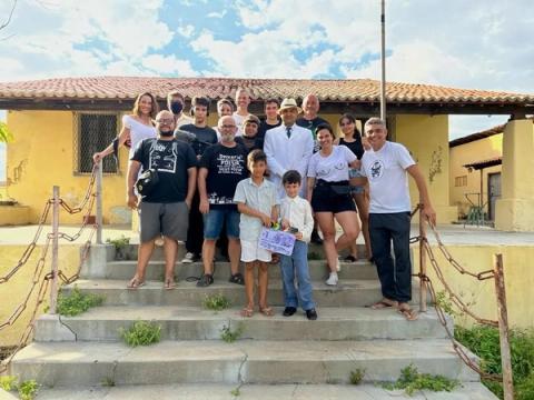 Grupo posando em escadas ao ar livre, com claquete sendo segurado por uma criança.