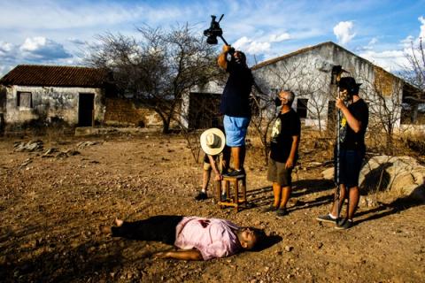 Pessoa sangrando no chão em área rural em uma cena, equipe filmando.